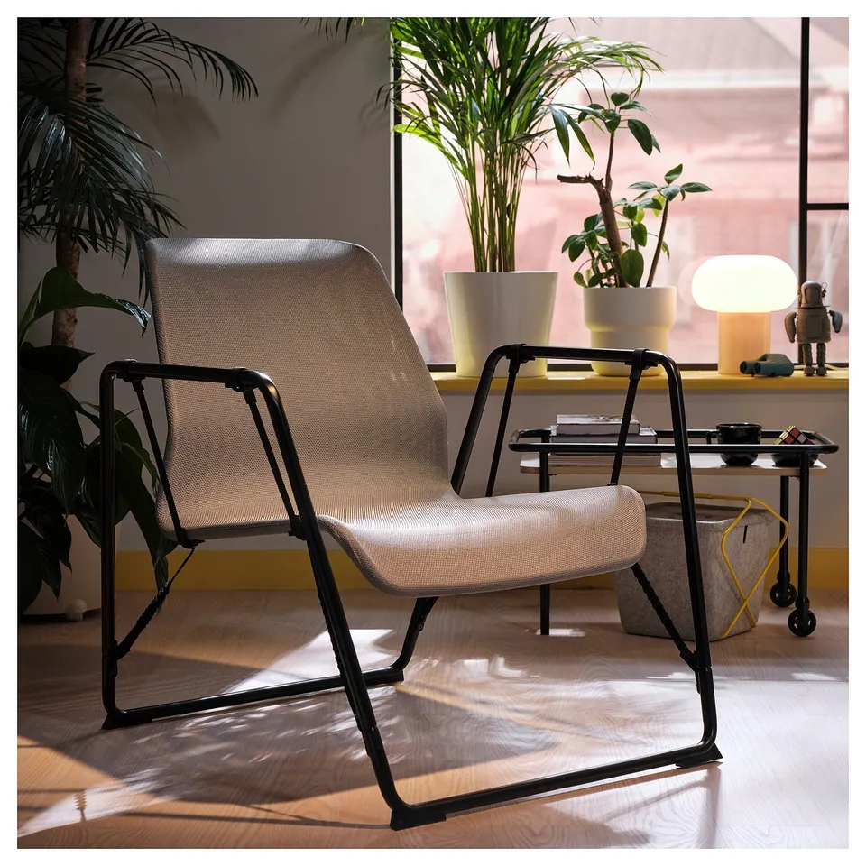 BRÄNNBOLL easy chair, black metal & beige fabric, sleek design, solitary by window, surrounded by plants & decor.