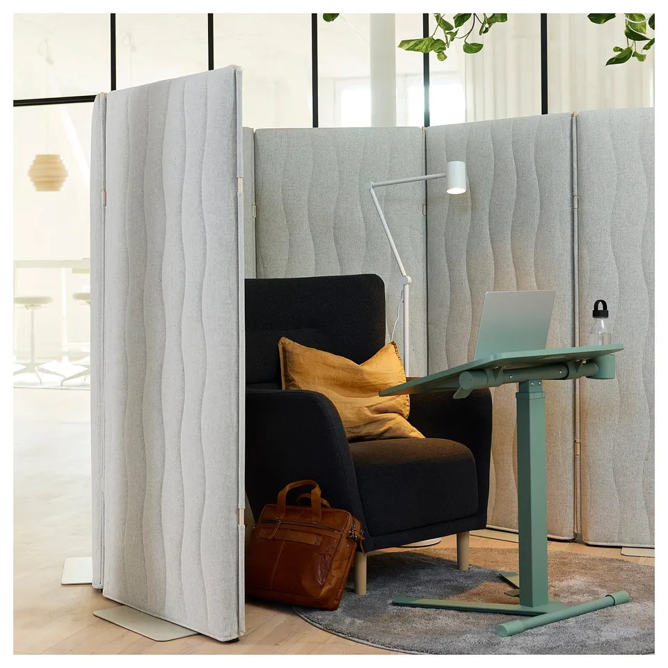 Home office setup with MITTZON grey acoustic screen, black chair, green desk, lamp, laptop, bag, and rug.