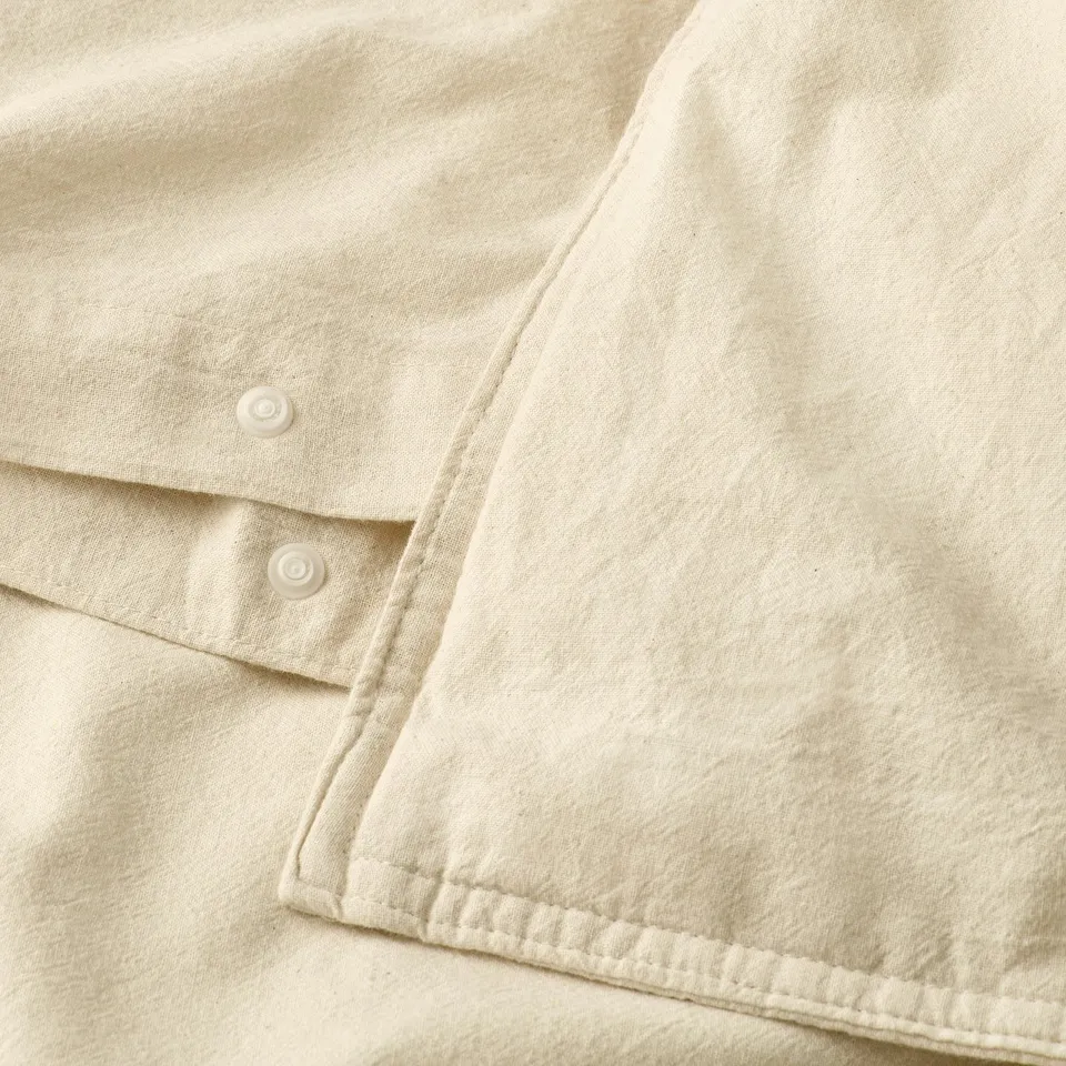 Close-up of cream-colored duvet with top button closure, showing soft fabric texture and stitching detail.