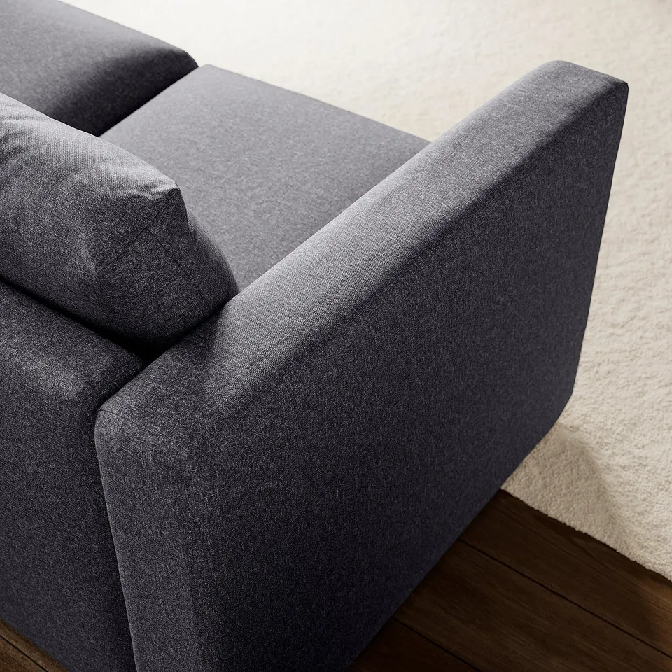 Modern grey sectional sofa, clean lines, soft cushions, placed on wooden floor, white wall behind.