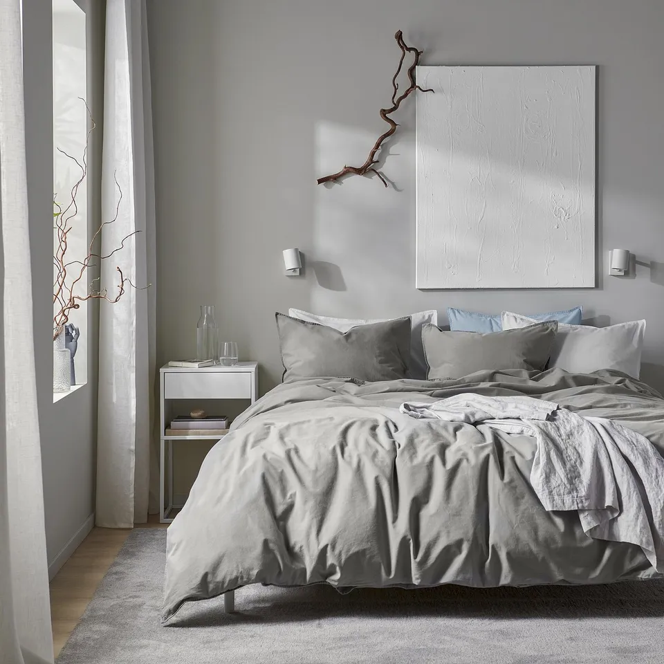 Bedroom with large grey ÄNGSLILJA duvet, soft washed cotton, large square pillowcases, white artwork, bedside with vases, minimalist design.
