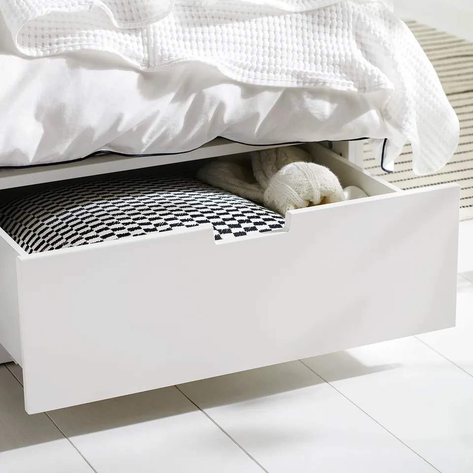 White under-bed storage drawer, partially open, filled with folded blanket and knitted items, viewed from side angle.