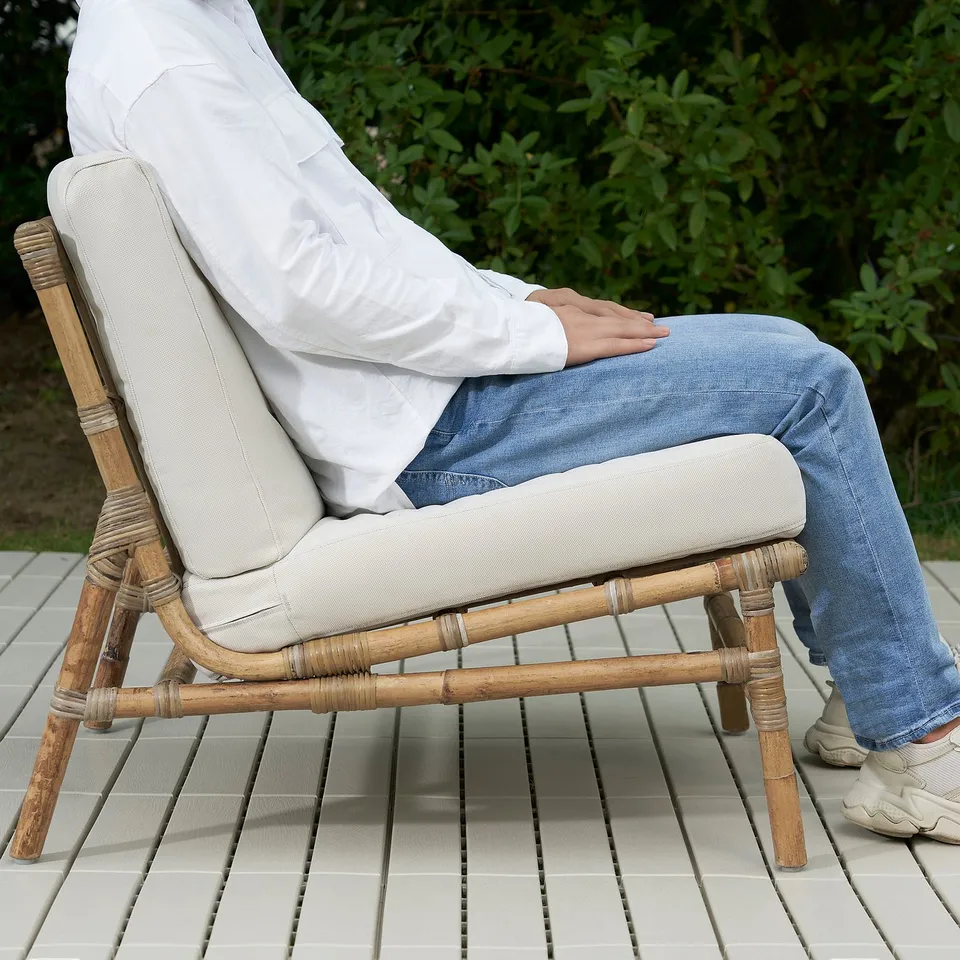 Person sitting on TVARÖ bamboo chair with cushion outdoors.