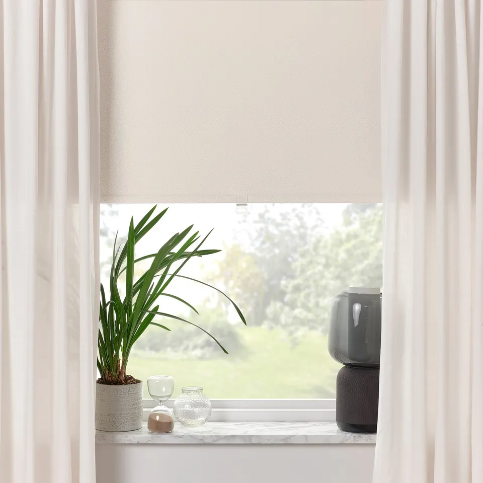 Window with roller blind partially drawn, displaying a peaceful outdoor scene. Plant and decor items are on the sill.