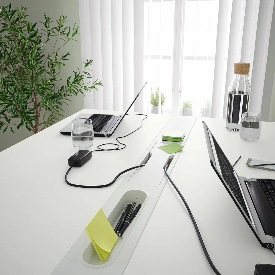 Modern conference table with power sockets, cable management, footrest, and pen storage for organised meetings.