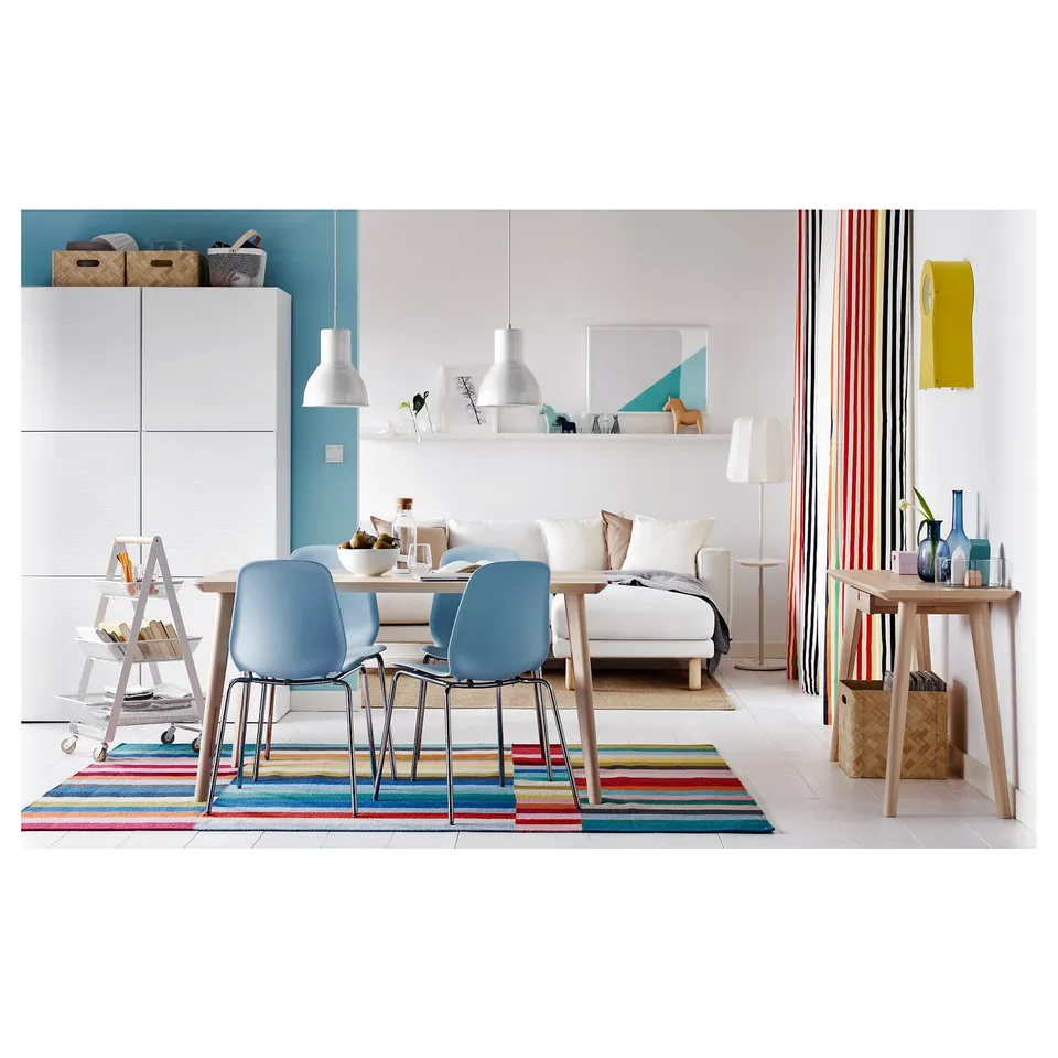 Bright, modern room with blue chairs, rainbow rug, white couch, colourful record divider, wooden table, and bookshelf with baskets.