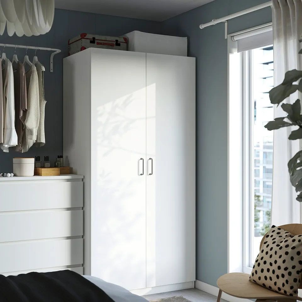 White PAX wardrobe in corner, sleek handles, blue room.