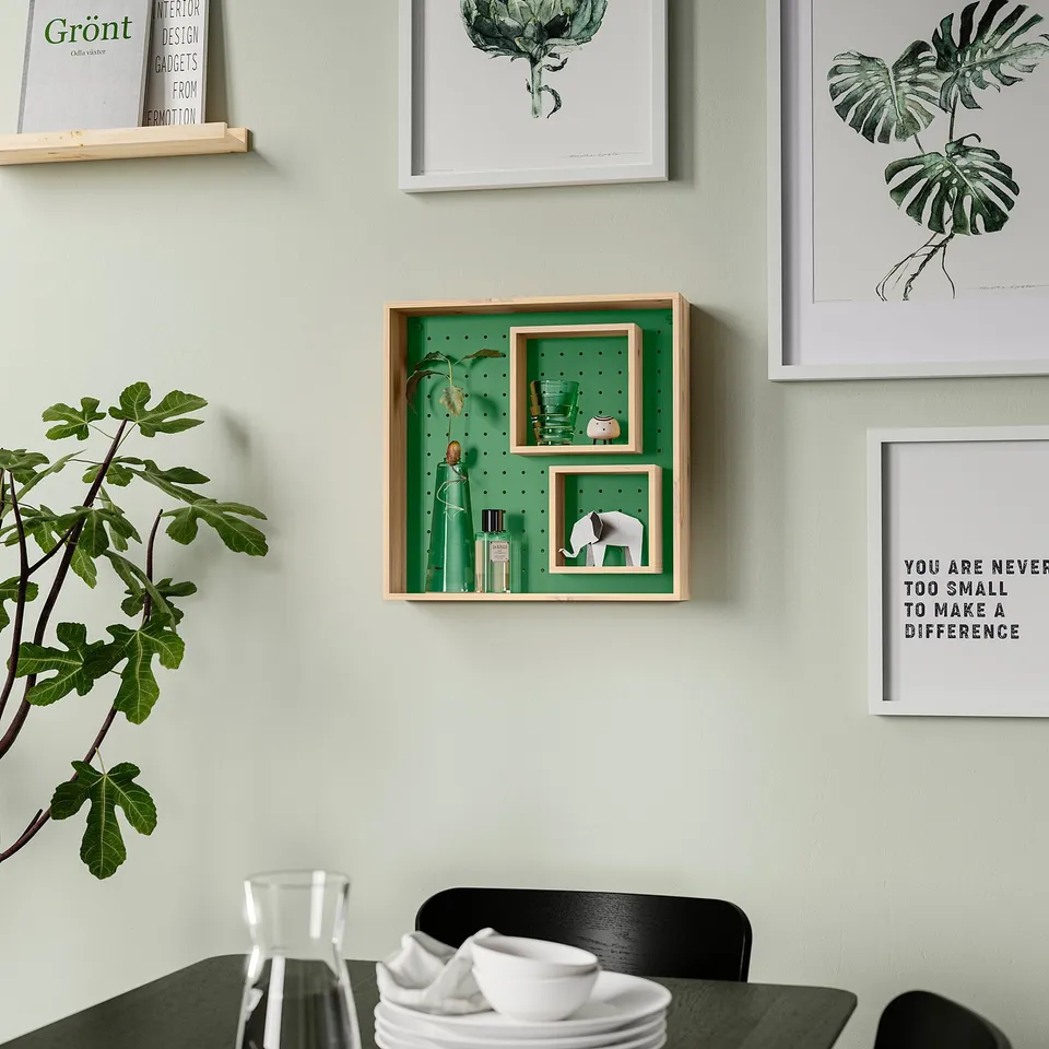 Green wall shelf with adjustable inner shelves, decorated with items and plants, surrounded by art and a black chair with crockery.