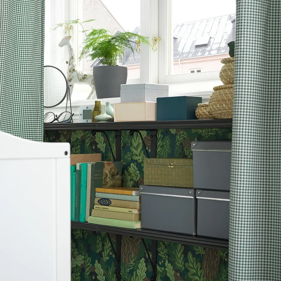 Black metal shelf with green leaf wallpaper, holding decorative boxes, books, and a fern plant.