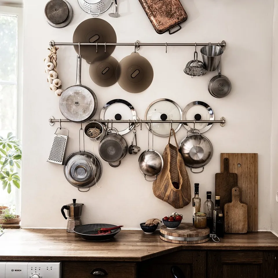 Kitchen with wooden counter, hanging pots, pans, lids, cutting boards, and a plant near a window.