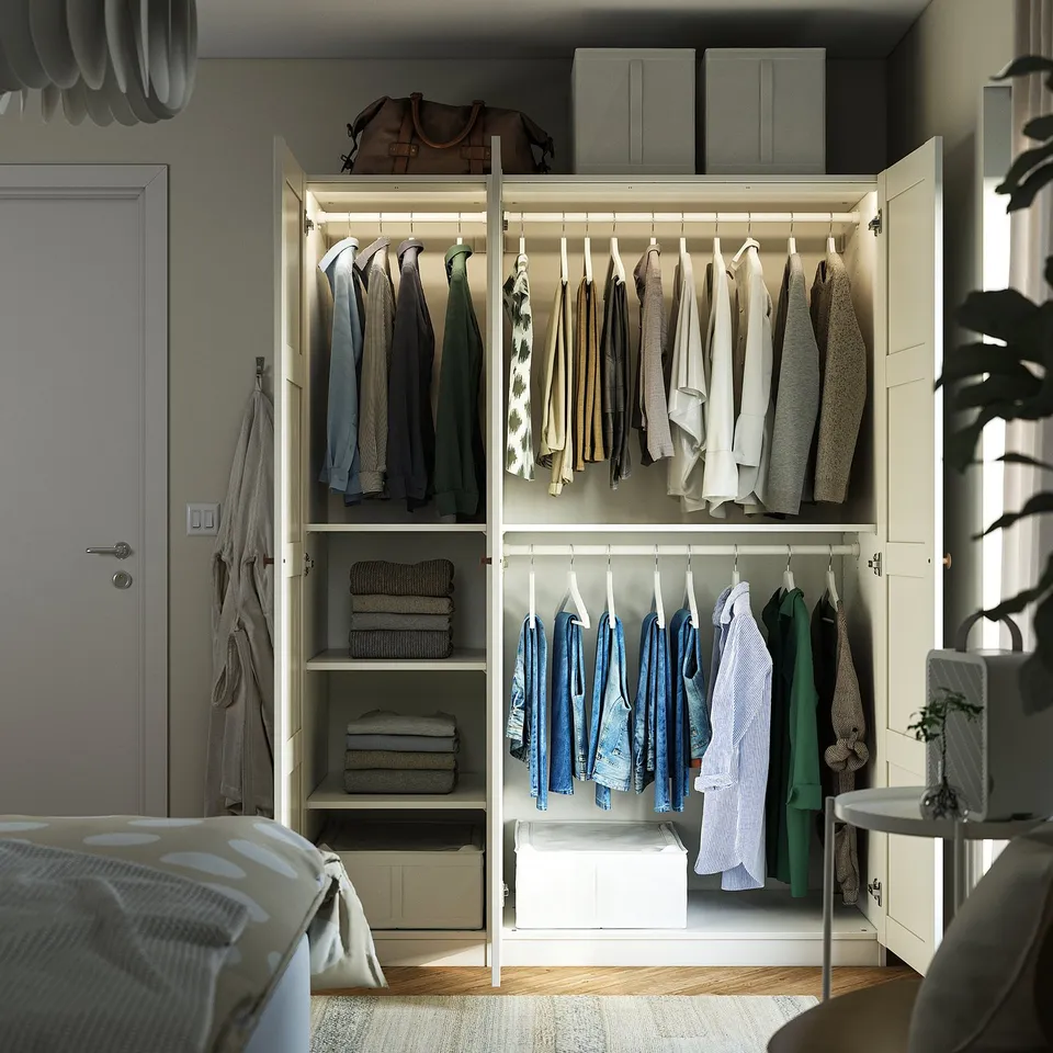 Bedroom with open wardrobe, clothes, shelves, boxes, and a plant.