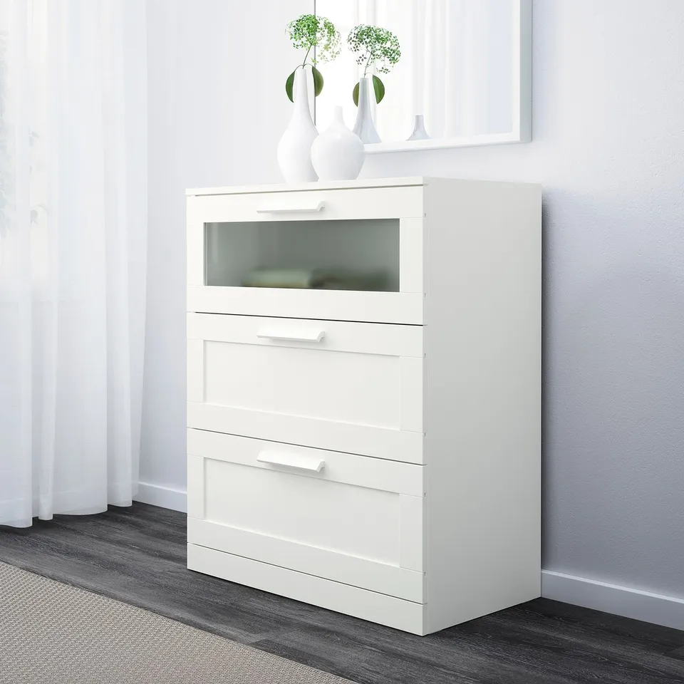 White chest with three drawers, top one glass, fits small spaces.