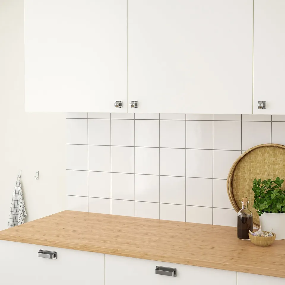 Kitchen counter with white cabinets and large square tiles. Wooden countertop, herbs, bowl, and olive oil displayed. Modern, functional design.