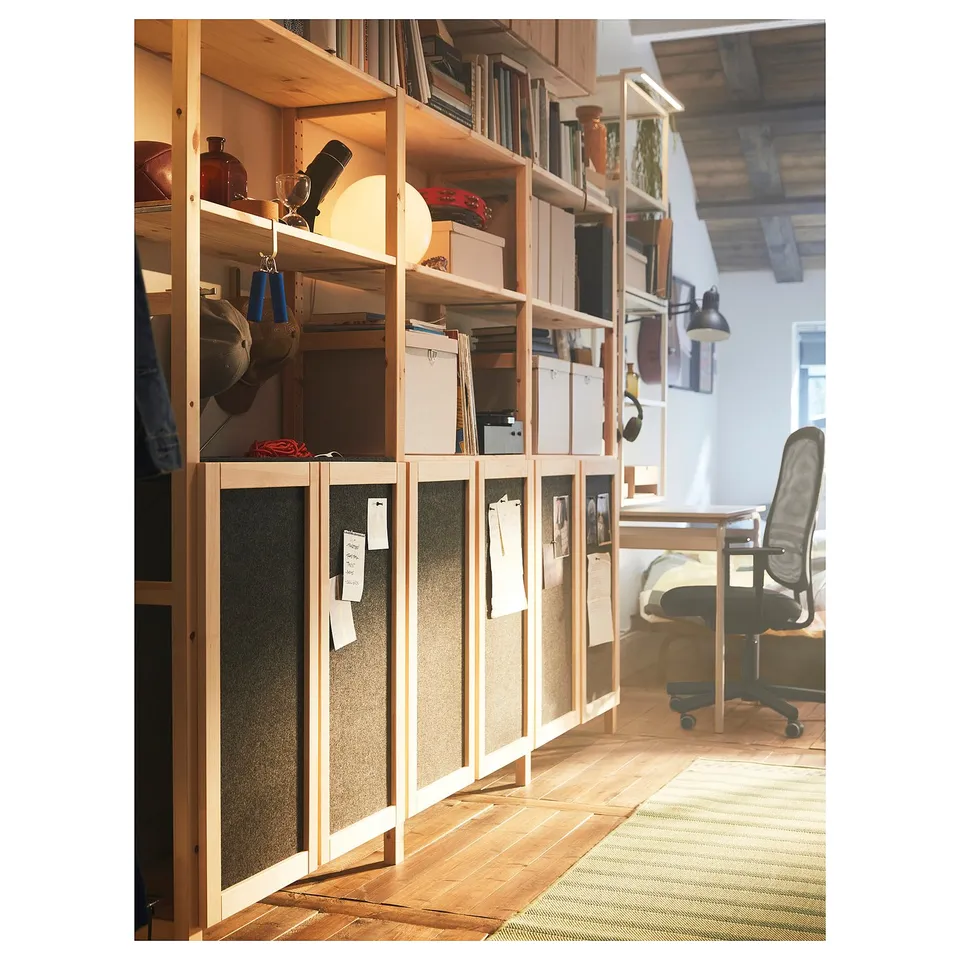 A wooden storage unit with felt doors, shelves with books, boxes, and decorative items. Light wood, soft design, a home office setup.