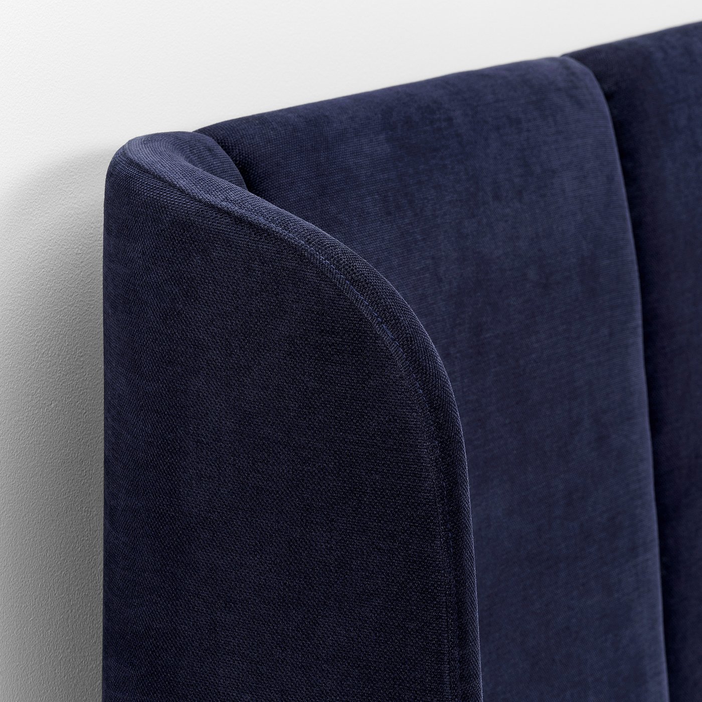 Close-up of dark blue upholstered bed headboard, showcasing soft, textured fabric and finely stitched edges.