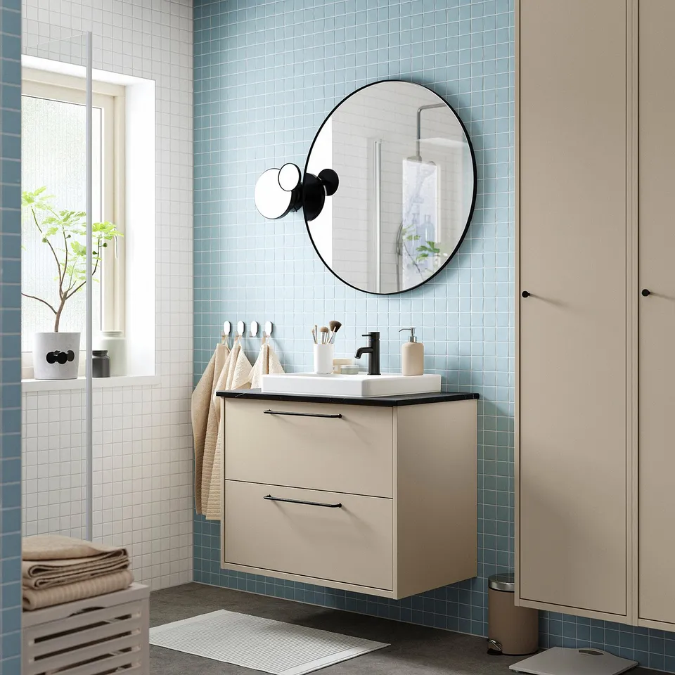 Modern bathroom with beige HAVBÄCK vanity, round mirror, blue tiles, and potted plant near window.