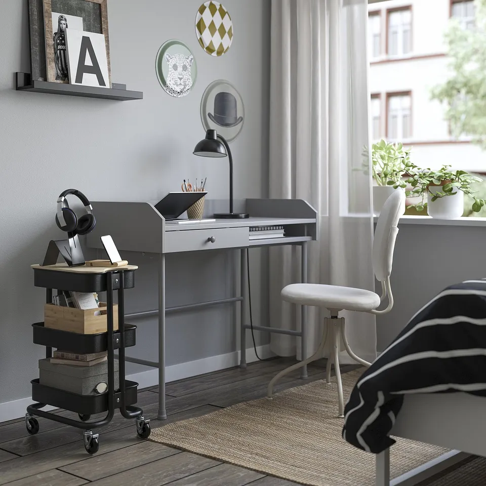Home office with RÅSKOG storage trolley, grey chair, desk, and city view.
