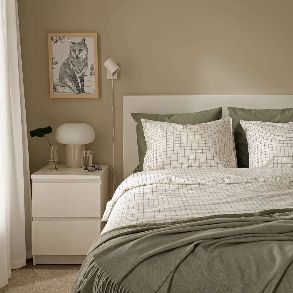 A cosy bed with a green DOFTAKLEJA duvet cover, white headboard, and matching pillowcases. A white bedside table with a lamp and a fox poster above.