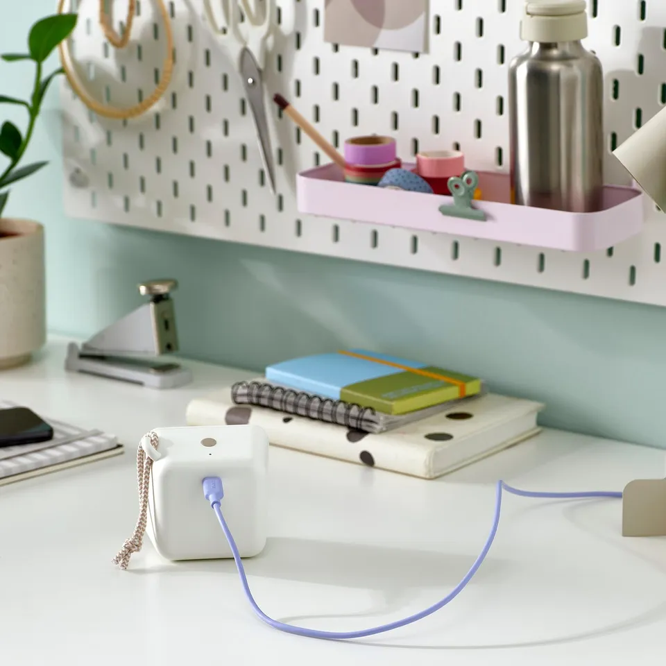 Desk with VAPPEBY portable speaker, notebooks, and office supplies. Speaker has blue cable, perfect for music on-the-go.
