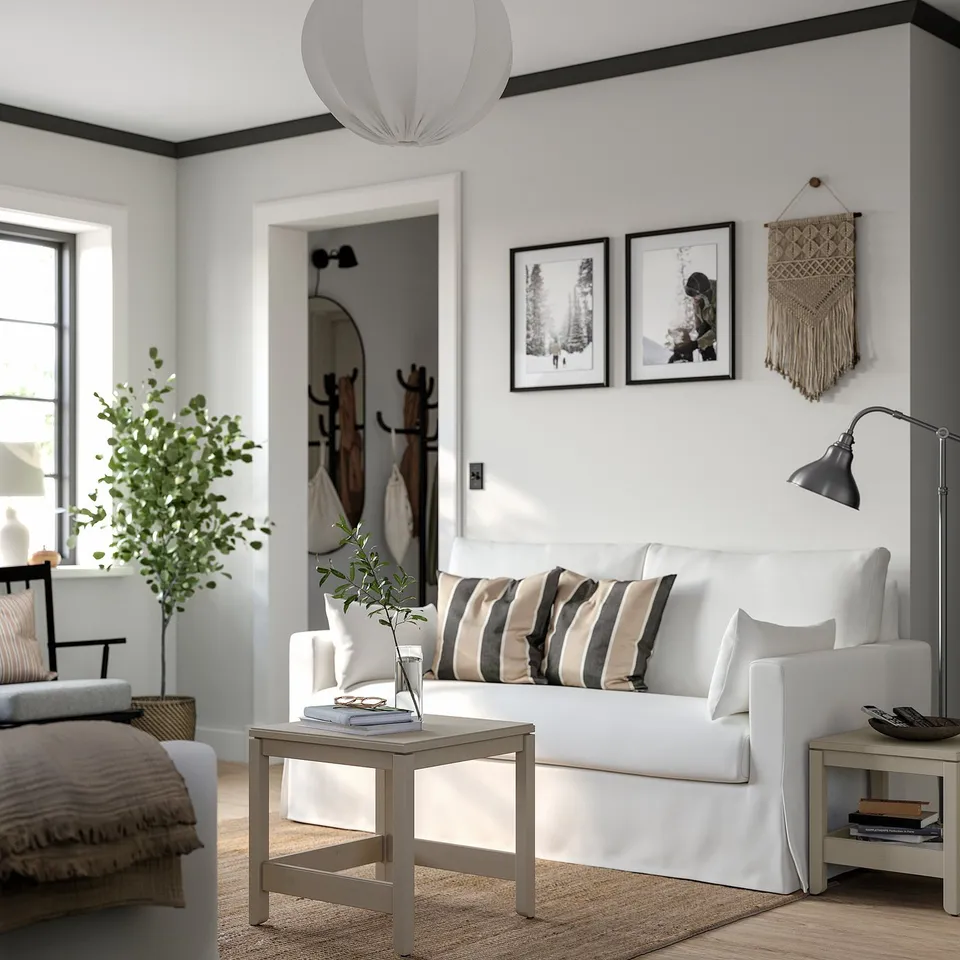 Clean, minimalist living room with a white HYLTARP sofa, striped cushions, wooden side table, large window, and wall hangings.