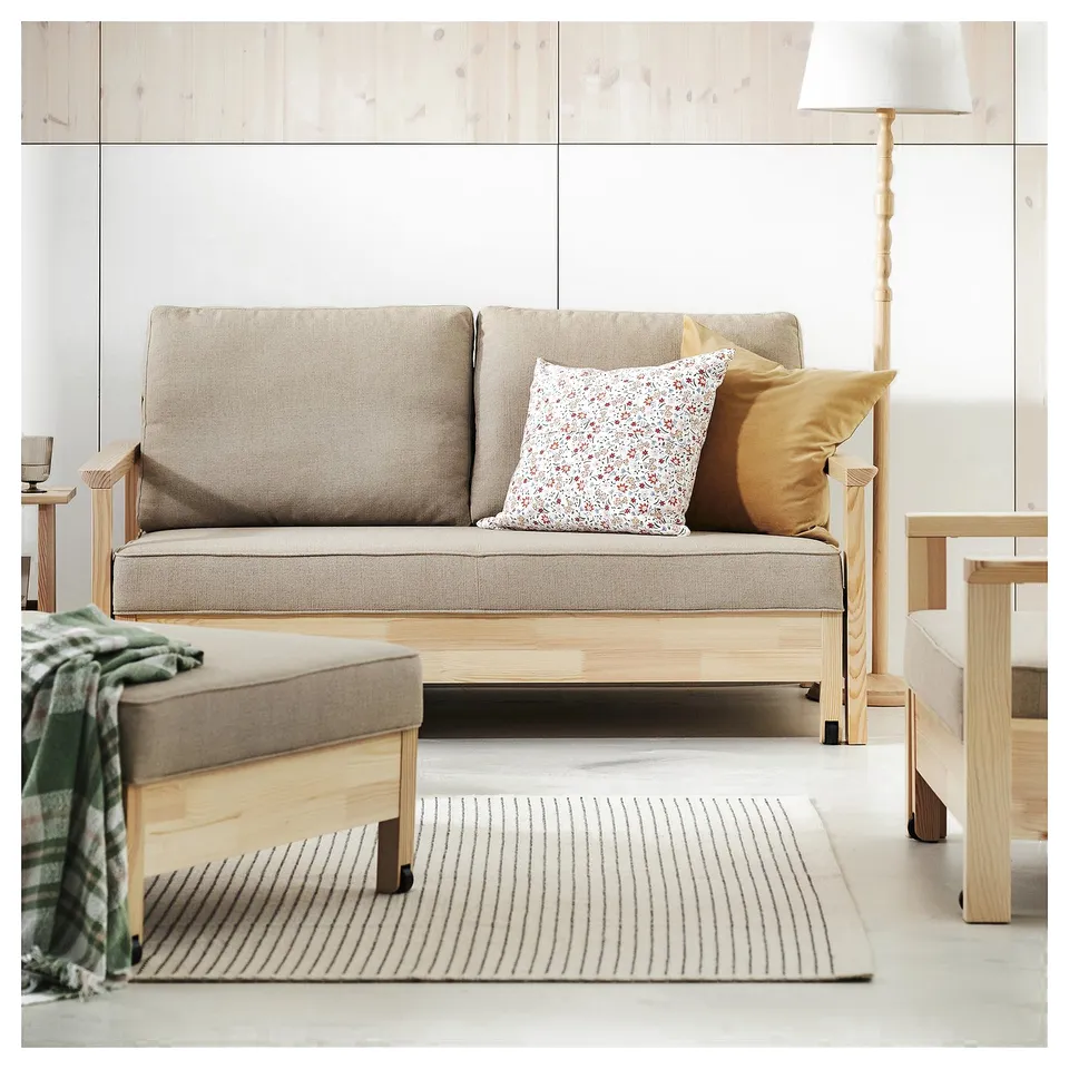 Minimalist living room with light grey sofa, wooden sides, and two pillows. Stripes rug beneath, lamp on the right.