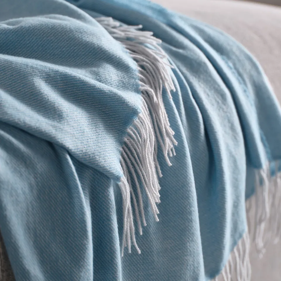 Light blue soft throw blanket with fringed edges draped over an object.