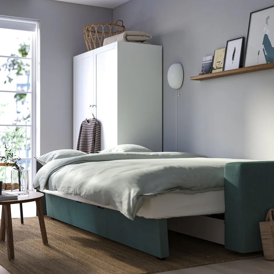 Minimalist bedroom with BÅRSLÖV sofa-bed, offering storage and quick bed conversion, against light blue wall.