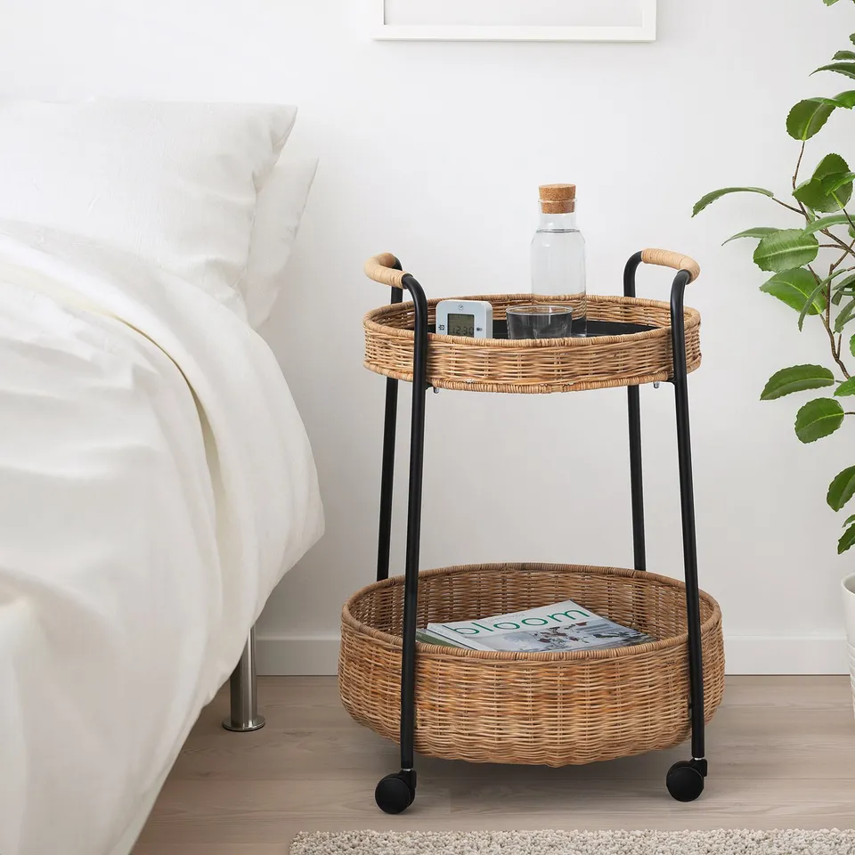 Wicker bedside table with baskets and black legs, beside bed.