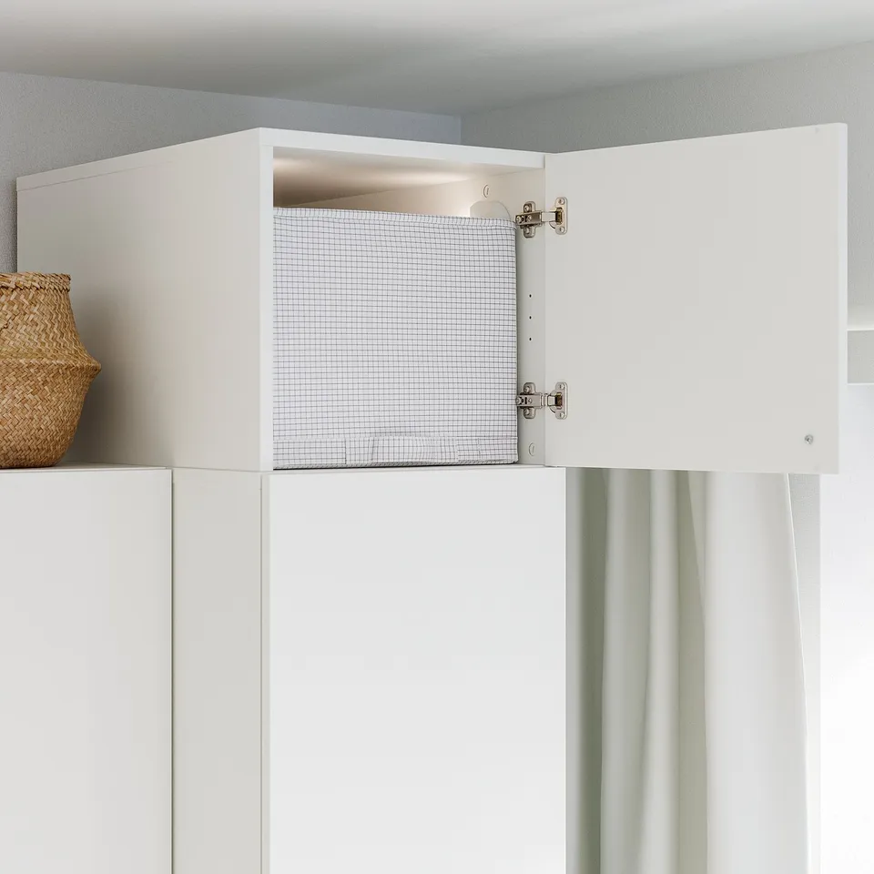 White cabinet with mesh-backed shelf, part of the LASTARE storage system, designed to fit seasonal items and taller spaces.