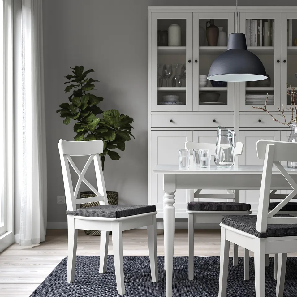 Modern dining room with white cross-back chairs, table setting, and stylish sideboard with greenery.