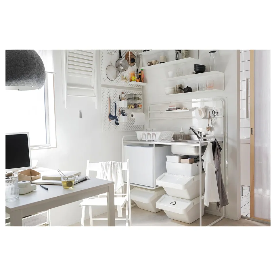 Compact white kitchen setup with stainless steel sink, open storage, and minimalistic design.