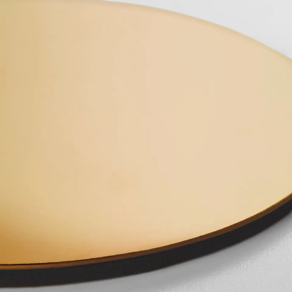 Gold-colored round coaster on a white surface, displaying a high-quality, reflective finish and a slim, dark edge.