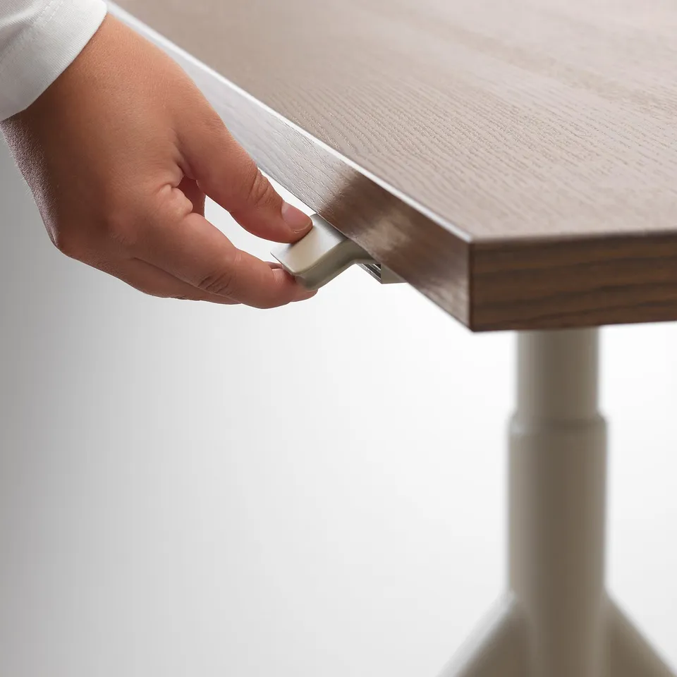 A hand adjusts a desks height using a handle, demonstrating its ergonomic feature.
