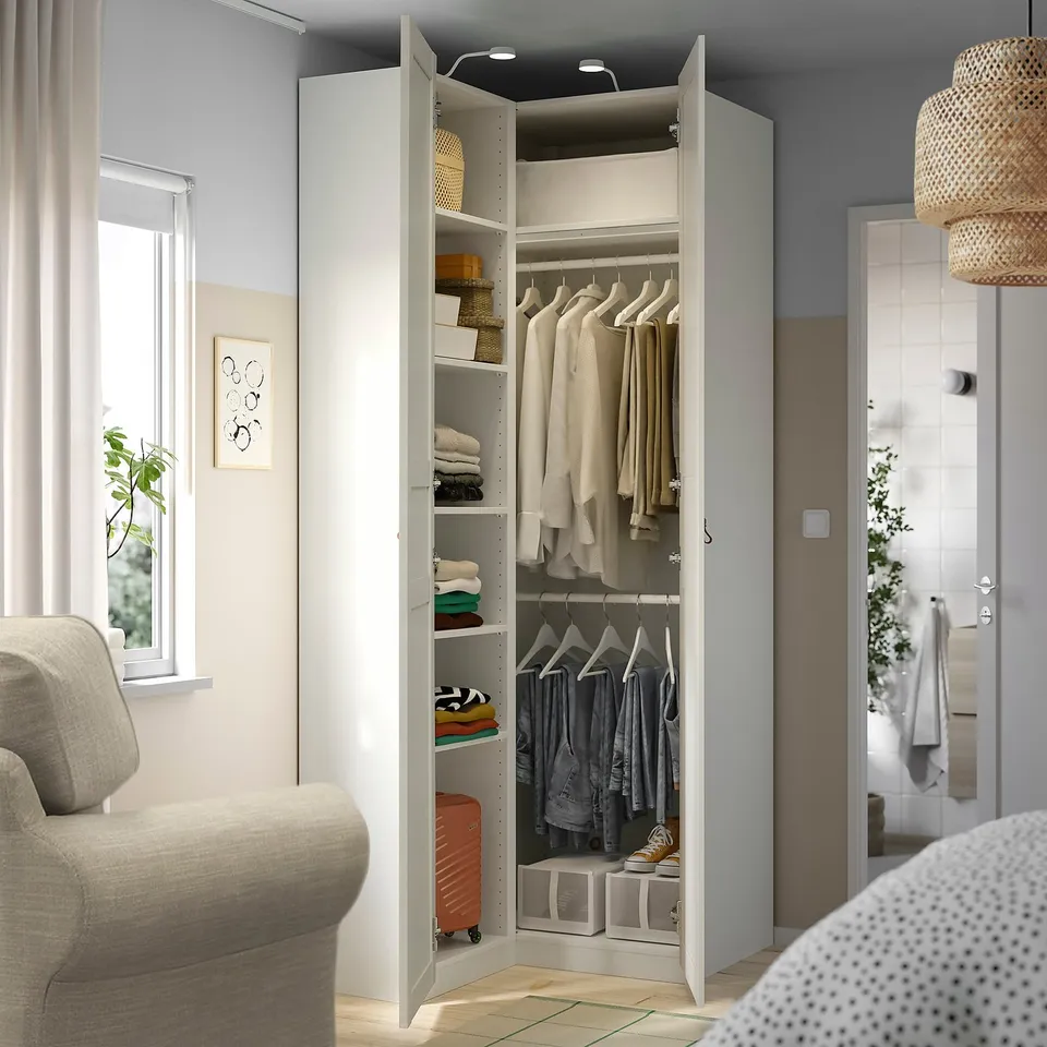 Open white corner wardrobe with clothes, shelves, and lighting.