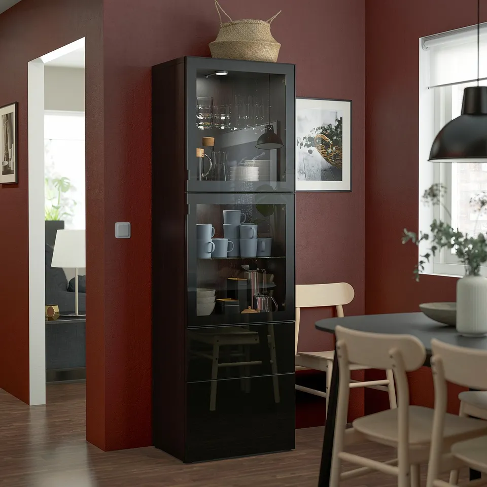 Black BESTÅ cabinet with glass doors in dining room, displaying cups and jars. Chairs and a table are around it.