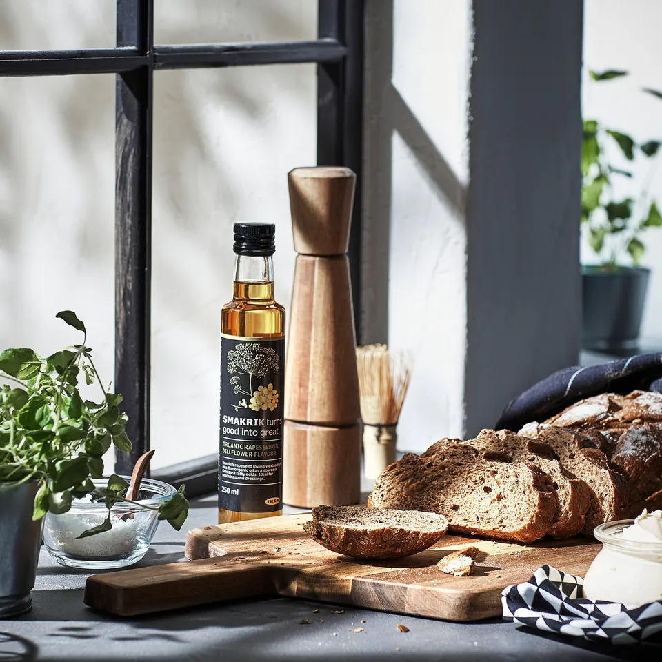 Wooden pepper mill on kitchen counter beside bread and oil.