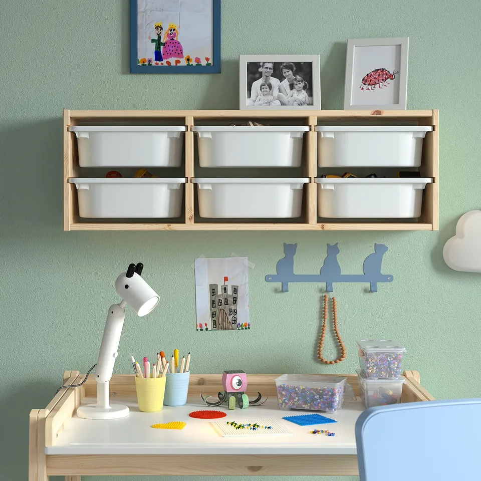Kids room with TROFAST wall storage, white. Wood frame, plastic bins. Hanging art, desk with lamp & toys.