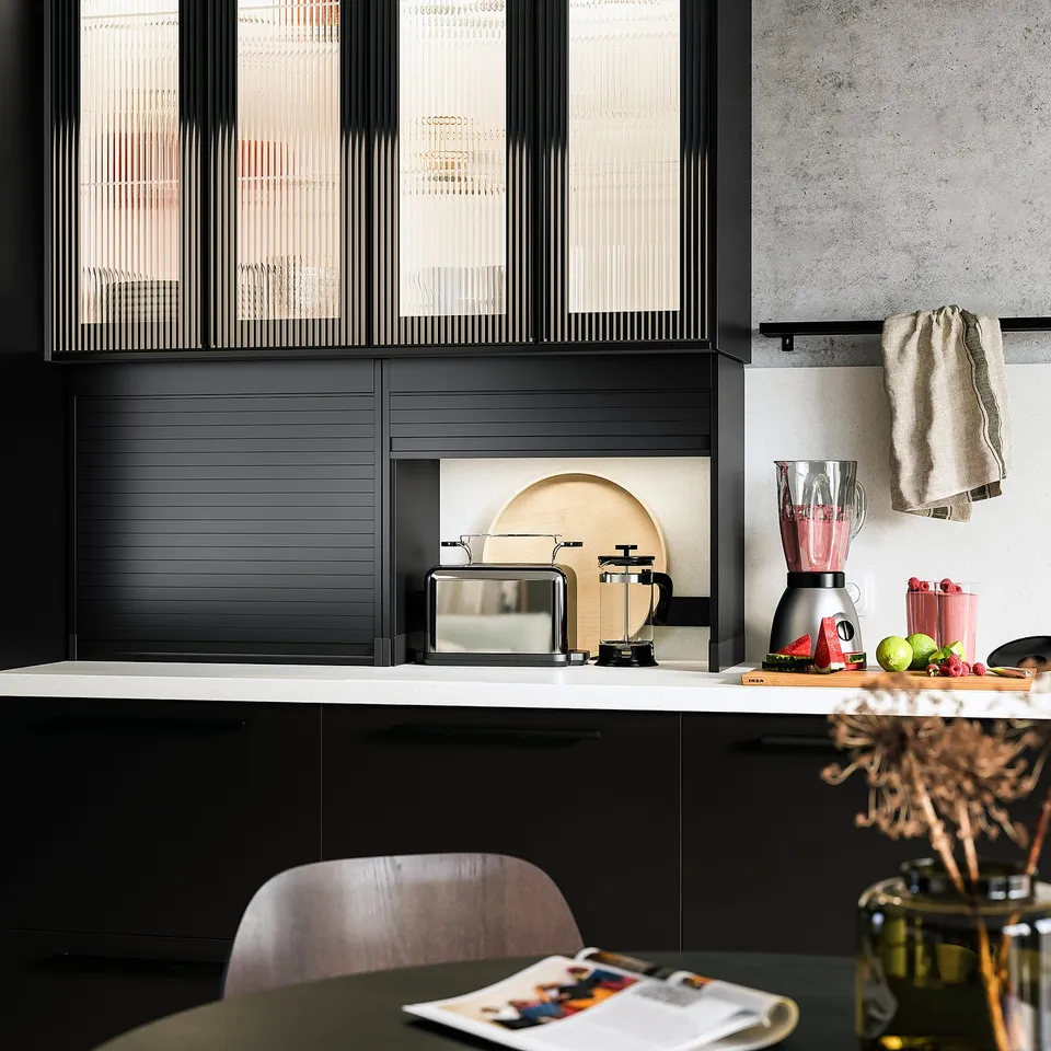Modern kitchen with black TITTEBO cabinets, appliances, fruits, towels, and a magazine on the table.