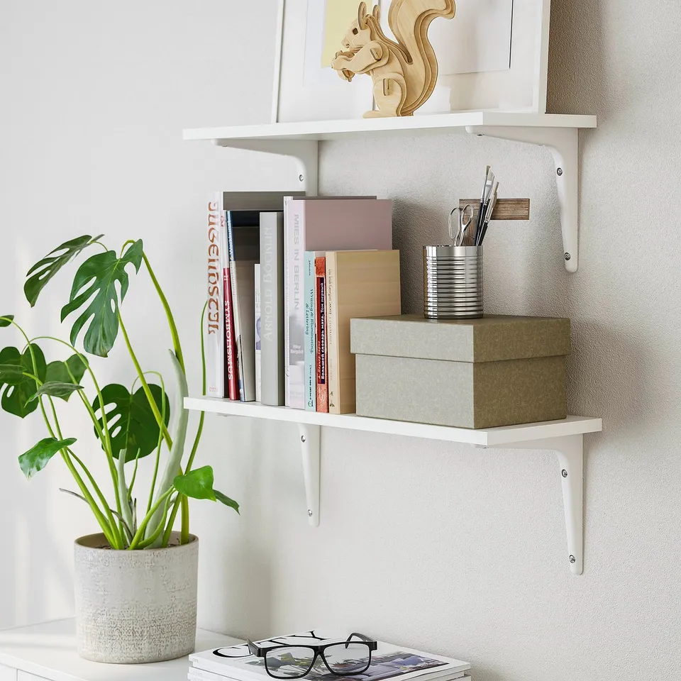 White wall shelf, BURHULT series, holding books, plant, and decor.
