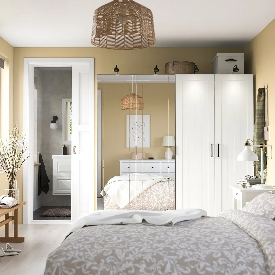 Modern bedroom with mirrored PAX wardrobe, pendant lamp, bedside table, and bed with neutral bedding.