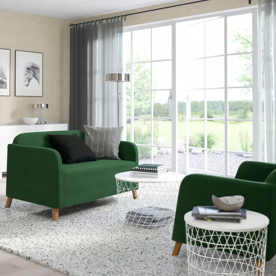 Bright living room with large windows, green couch and chair, white tables, grey rug, black and white art, and sheers.