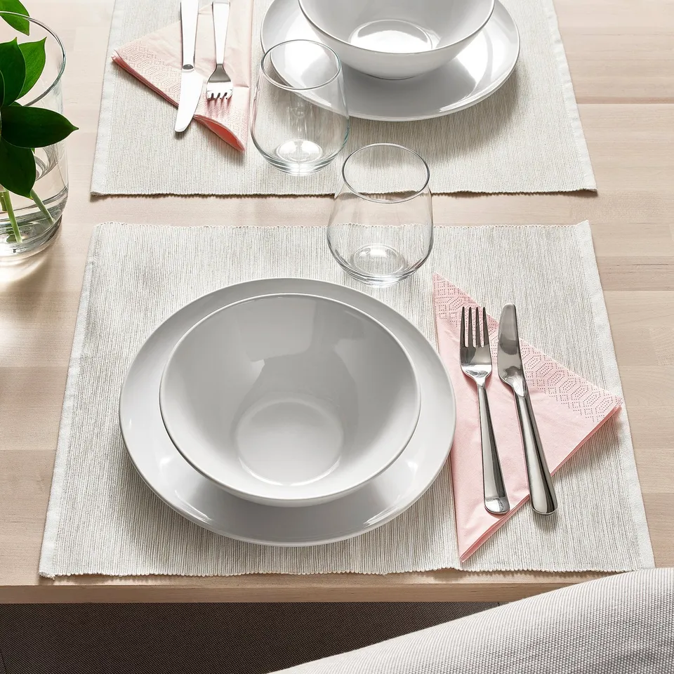 Two table settings with white plates, bowls, glasses, cutlery, and pink napkins on beige placemats.