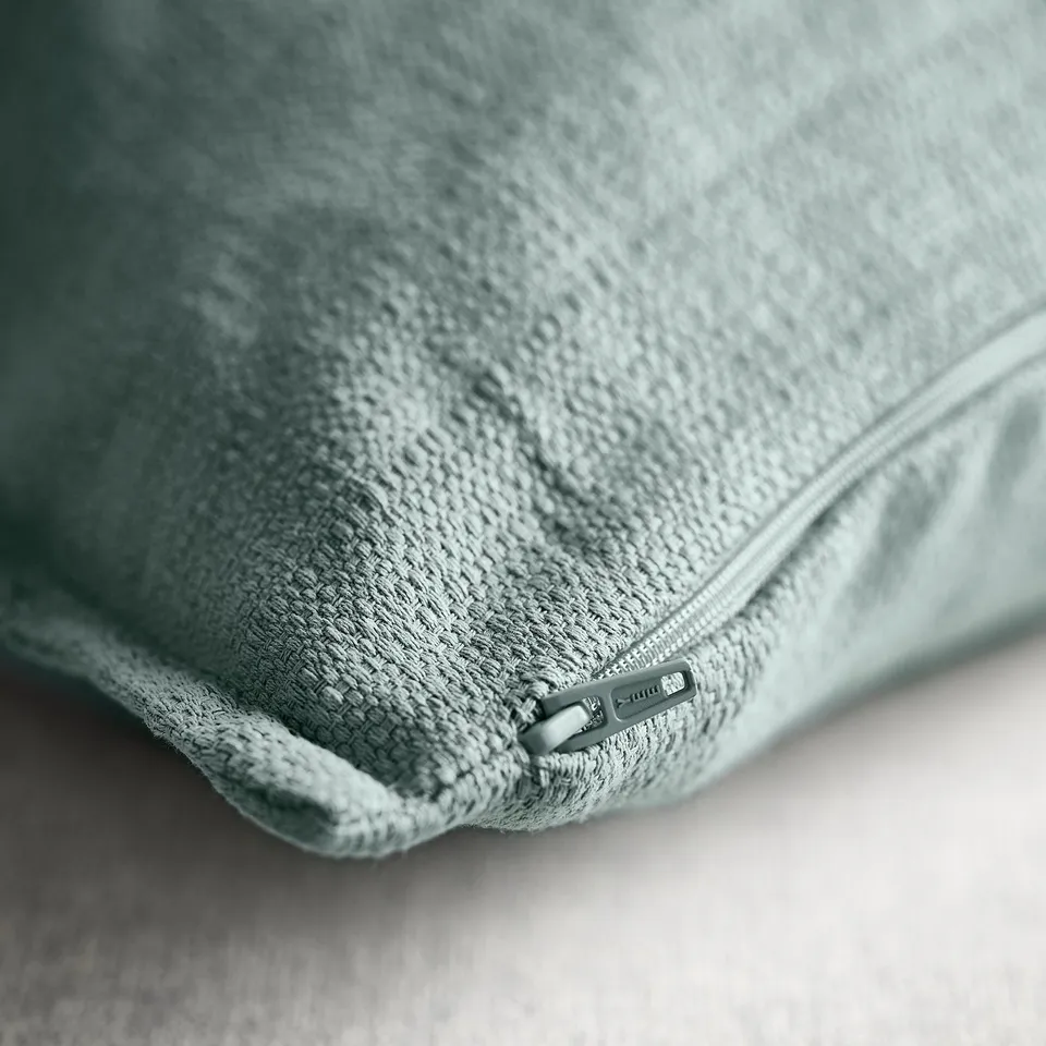 Close-up of light blue-grey cushion cover with zip, showcasing textured, matte-sheen fabric.