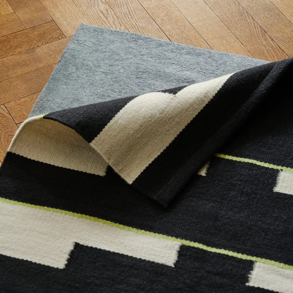 Handwoven wool rug with reversible geometric pattern on wooden floor.