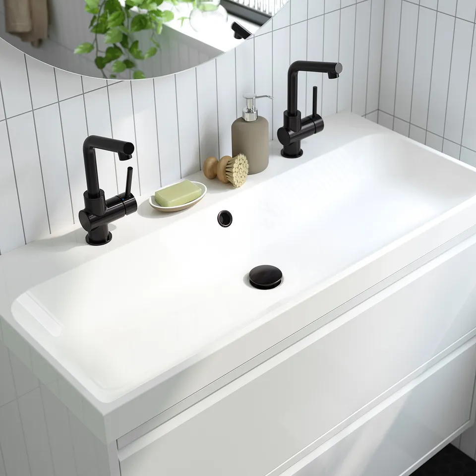 Modern bathroom sink with integrated marble basin, two sleek black faucets, soap, and brush. Clean, minimalist design with ample counter space.