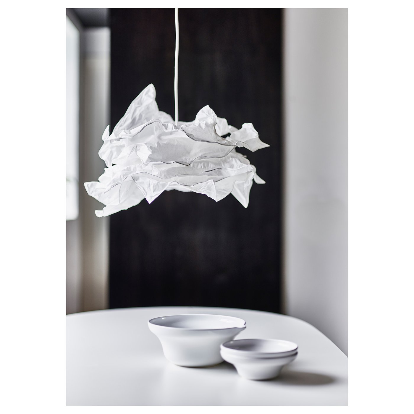 Unique pendant lamp with crumpled paper design, casting soft diffused light above white ceramic bowls on a table.
