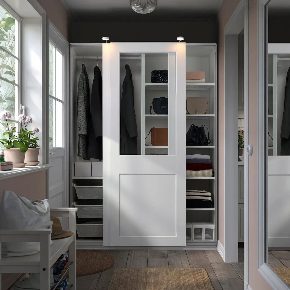 White PAX wardrobe with sliding glass doors, organised clothes, built-in lights.