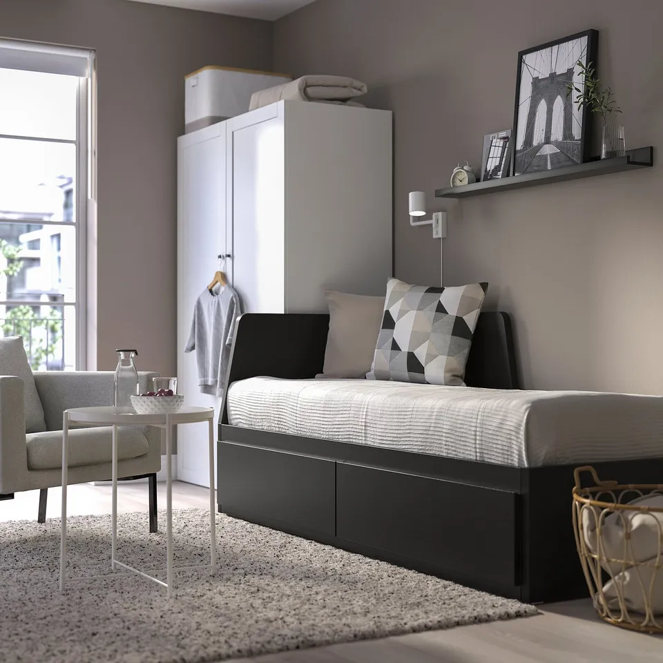 Modern bedroom with FLEKKE sofa-bed & storage, grey armchair, minimalist decor.