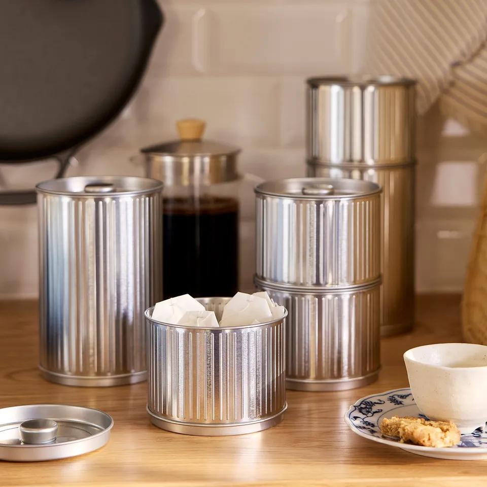 Silver metal BETTHAJ tins of varying sizes on a countertop with coffee and cookies. One open displaying sugar cubes.