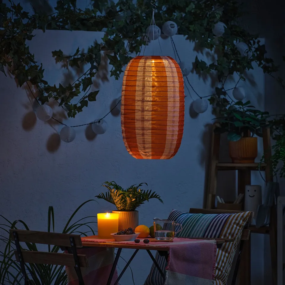 Cosy outdoor space lit by SOLVINDEN solar-powered lantern and candles on table.